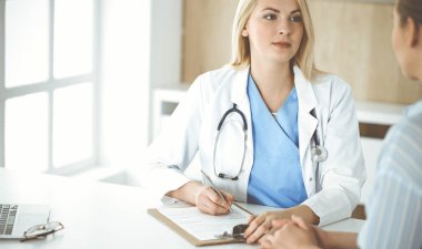 Kadın doktor ve hasta hastanede ya da klinikte oturup konuşuyorlar. Sarışın terapist neşeyle gülümsüyor. Tıp konsepti