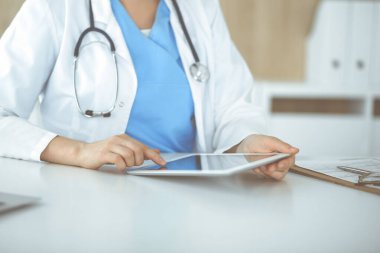 Bilinmeyen kadın doktor klinikte duruyor ve tablet bilgisayar kullanıyor, yakın plan. Veriler ve tıp ve sağlık hizmetlerindeki en iyi hizmet