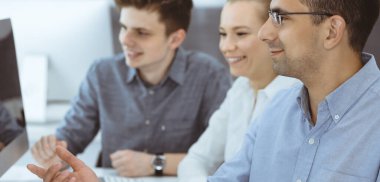 Modern ofiste birlikte çalışan iş adamları. Mutlu gülümseyen yetişkin iş adamı meslektaşlarıyla bilgisayar kullanıyor. Takım çalışması ve ortaklık kavramı