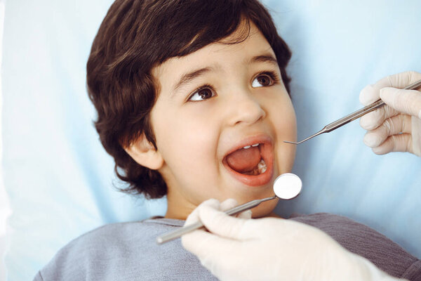 Милый арабский мальчик сидит в стоматологическом кресле с открытым ртом во время орального осмотра у врача. Посещение кабинета дантиста. Концепция стоматологии