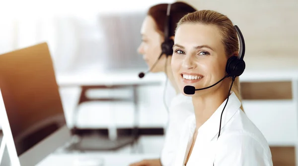 Blond female customer service representative is consulting clients online using headset in sunny office. Call center concept