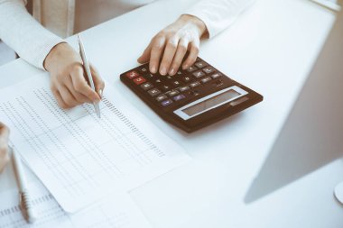 Muhasebeci mali durumu kontrol ediyor ya da vergi formları için hesap makinesi geliri ile sayıyor, eller yakın çekim. İş kadını ofisteki masada iş arkadaşıyla oturuyor ve çalışıyor. Denetim kavramı