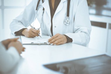 Bilinmeyen kadın-doktor ve kadın hasta klinikteki tıbbi muayenede oturuyor ve konuşuyor, yakın plan. Yeşil bluz giyen terapist ilaç geçmişini dolduruyor. Tıp konsepti