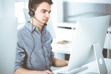İnternette müşterilerle konuşurken kulaklık ve bilgisayar kullanan sıradan giyinmiş genç bir adam. Çağrı merkezi, iş konsepti