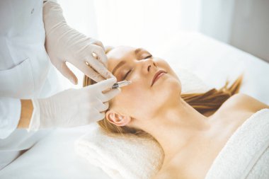 Güzellik doktoru sarışın kadın yüzüne şırıngayla güzellik prosedürü uyguluyor. Kozmetik tıp, güzellik enjeksiyonu konsepti