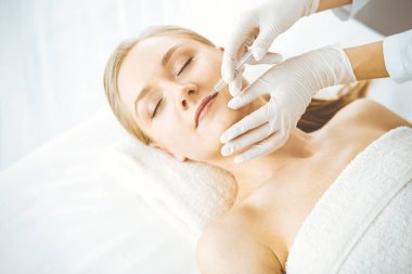 Güzellik doktoru sarışın kadın yüzüne şırıngayla güzellik prosedürü uyguluyor. Kozmetik tıp, güzellik enjeksiyonu konsepti