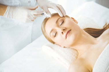 Güzellik doktoru sarışın kadın yüzüne şırıngayla güzellik prosedürü uyguluyor. Kozmetik tıp, güzellik enjeksiyonu konsepti