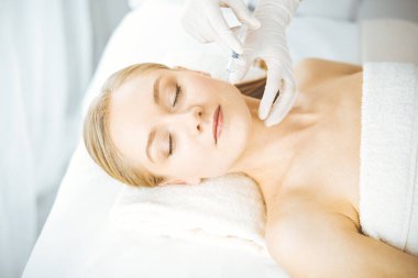 Güzellik doktoru sarışın kadın yüzüne şırıngayla güzellik prosedürü uyguluyor. Kozmetik tıp, güzellik enjeksiyonu konsepti