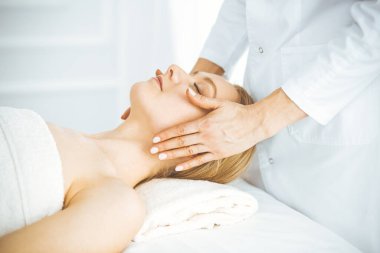 Güzel, mutlu bir kadın kaplıca salonunda kapalı gözlerle yüz masajından zevk alıyor. Tıp ve Güzellik konseptinde rahatlatıcı tedavi