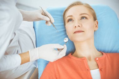 Mutlu gülümseyen kadın dişçi kliniğinde dişçi tarafından muayene ediliyor. Sağlıklı dişler ve ilaçlar, stomatoloji konsepti