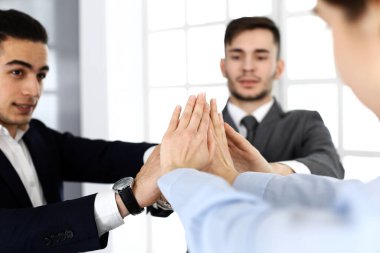 İş adamları grubu takım çalışması sergiliyor, el ele tutuşuyor ve modern ofiste birbirlerine beş tane veriyorlar. Başarı konsepti