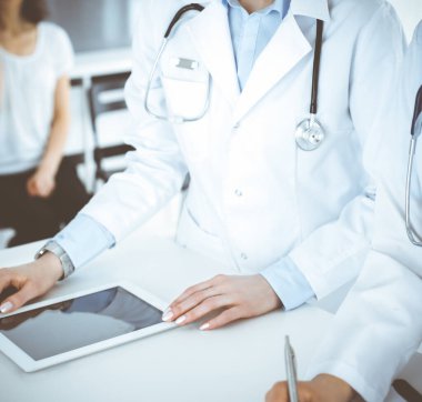 Arka planda hastası olan iki kadın doktor var. Resepsiyonda tıbbi belgeleri dolduran kadın doktorlar, yakın çekim. Tıptaki veriler