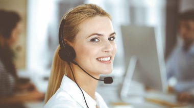 Sarışın iş kadını iletişim kurmak ve müşteri hizmetlerindeki insanlara danışmak için kulaklık kullanıyor. Merkezi ara. Bir grup operatör iş başında