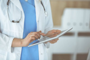 Bilinmeyen kadın doktor klinikte duruyor ve tablet bilgisayar kullanıyor, yakın plan. Veriler ve tıp ve sağlık hizmetlerindeki en iyi hizmet