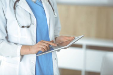 Bilinmeyen kadın doktor klinikte duruyor ve tablet bilgisayar kullanıyor, yakın plan. Veriler ve tıp ve sağlık hizmetlerindeki en iyi hizmet