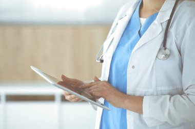 Bilinmeyen kadın doktor klinikte duruyor ve tablet bilgisayar kullanıyor, yakın plan. Tıp ve sağlık alanlarındaki veriler