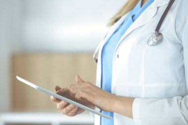 Bilinmeyen kadın doktor klinikte duruyor ve tablet bilgisayar kullanıyor, yakın plan. Tıp ve sağlık alanlarındaki veriler