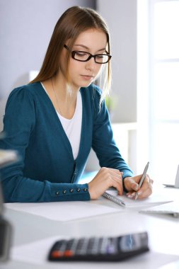 Muhasebeci mali durumu kontrol ediyor ya da vergi formları için hesap makinesi geliri ile sayıyor, eller yakın çekim. Ofisteki masada oturan ve çalışan bir iş kadını. Denetim kavramı