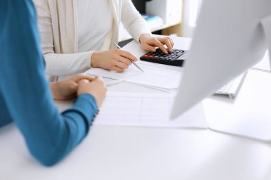 Muhasebeci mali durumu kontrol ediyor ya da vergi formları için hesap makinesi geliri ile sayıyor, eller yakın çekim. İş kadını ofisteki masada iş arkadaşıyla oturuyor ve çalışıyor. Denetim kavramı