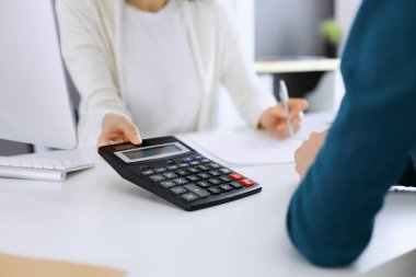 Muhasebeci mali durumu kontrol ediyor ya da vergi formları için hesap makinesi geliri ile sayıyor, eller yakın çekim. İş kadını ofisteki masada iş arkadaşıyla oturuyor ve çalışıyor. Denetim kavramı