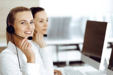 Sarışın kadın müşteri hizmetleri temsilcisi ve meslektaşı internetteki müşterilerine kulaklık kullanarak danışıyorlar. Çağrı merkezi ve iş adamları kavramı