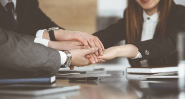 Bilinmeyen iş adamları modern ofiste el ele tutuşuyor. İş adamları ve kadınlar elleriyle bir takım olarak daire çiziyorlar, yakın plan.