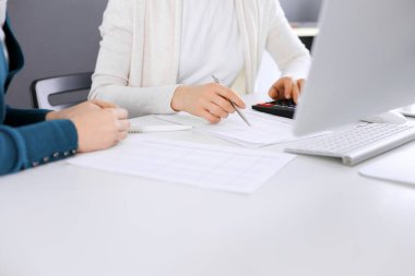 Muhasebeci mali durumu kontrol ediyor ya da vergi formları için hesap makinesi geliri ile sayıyor, eller yakın çekim. İş kadını ofisteki masada iş arkadaşıyla oturuyor ve çalışıyor. Denetim kavramı