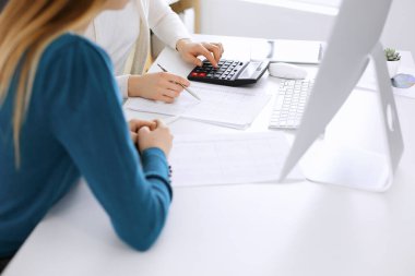 Muhasebeci mali durumu kontrol ediyor ya da vergi formları için hesap makinesi geliri ile sayıyor, eller yakın çekim. İş kadını ofisteki masada iş arkadaşıyla oturuyor ve çalışıyor. Denetim kavramı