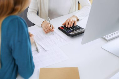 Muhasebeci mali durumu kontrol ediyor ya da vergi formları için hesap makinesi geliri ile sayıyor, eller yakın çekim. İş kadını ofisteki masada iş arkadaşıyla oturuyor ve çalışıyor. Denetim kavramı