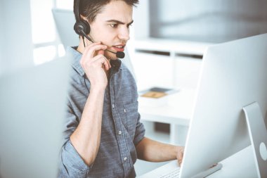 İnternette müşterilerle konuşurken kulaklık ve bilgisayar kullanan sıradan giyinmiş genç bir adam. Çağrı merkezi, iş konsepti