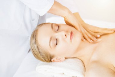 Güzel beyaz kadın güneşli spa salonunda kapalı gözlerle yüz masajından hoşlanıyor. İlaçta rahatlatıcı tedavi