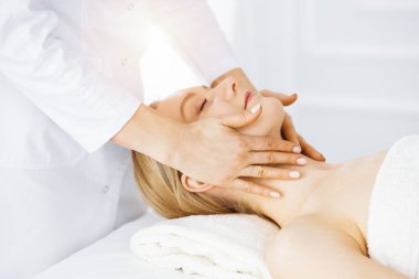 Güzel beyaz kadın güneşli spa salonunda kapalı gözlerle yüz masajından hoşlanıyor. İlaçta rahatlatıcı tedavi