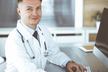 Klinikte ya da hastane ofisinde bilgisayar başında oturan bir doktor. Tıbbi vesikalık ve tıp konsepti