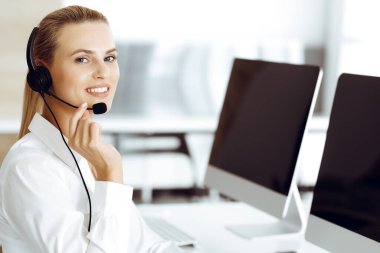 Sarışın kadın müşteri hizmetleri temsilcisi müşterilerine kulaklık kullanarak danışmanlık yapıyor. Çağrı merkezi ve iş konsepti