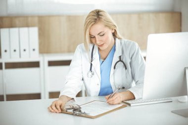 Hastanedeki ya da klinikteki masa başında oturan kadın doktor. Sarışın, neşeli doktor ilaç geçmişi formunu dolduruyor.