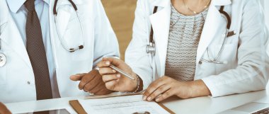 İki bilinmeyen doktor hastane ofisinde masa başında otururken tedavi sorunlarını tartışıyor, yakın plan. Tıptaki veriler