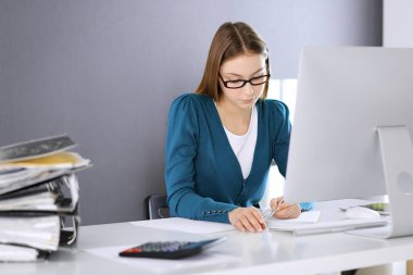 Muhasebeci mali durumu kontrol ediyor ya da vergi formları için hesap makinesi geliri ile sayıyor, eller yakın çekim. Ofisteki masada oturan ve çalışan bir iş kadını. Denetim kavramı