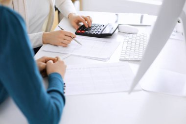 Muhasebeci mali durumu kontrol ediyor ya da vergi formları için hesap makinesi geliri ile sayıyor, eller yakın çekim. İş kadını ofisteki masada iş arkadaşıyla oturuyor ve çalışıyor. Denetim kavramı