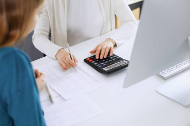 Muhasebeci mali durumu kontrol ediyor ya da vergi formları için hesap makinesi geliri ile sayıyor, eller yakın çekim. İş kadını ofisteki masada iş arkadaşıyla oturuyor ve çalışıyor. Denetim kavramı