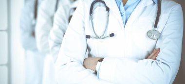 Bir grup modern doktor hastane ofisinde kollarını kavuşturmuş bir takım gibi duruyorlar. Tıbbi yardım, sağlık sigortası, en iyi hastalık tedavisi ve ilaç konsepti