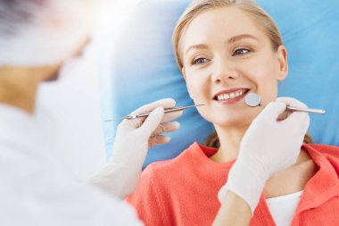 Mutlu gülümseyen kadın dişçi kliniğinde dişçi tarafından muayene ediliyor. Sağlıklı dişler ve ilaçlar, stomatoloji konsepti