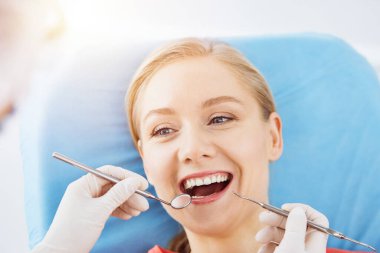 Mutlu gülümseyen kadın dişçi kliniğinde dişçi tarafından muayene ediliyor. Sağlıklı dişler ve ilaçlar, stomatoloji konsepti