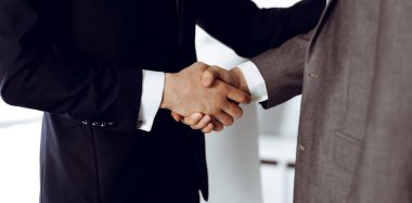 Bilinmeyen işadamı, modern ofiste dikilirken iş arkadaşı ya da ortağıyla el sıkışıyor. Toplantıda iş adamları grubu