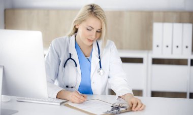 Hastanedeki ya da klinikteki masa başında oturan kadın doktor. Sarışın, neşeli doktor ilaç geçmişi formunu dolduruyor.