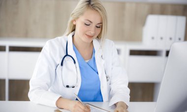 Hastanedeki ya da klinikteki masa başında oturan kadın doktor. Sarışın, neşeli doktor ilaç geçmişi formunu dolduruyor.