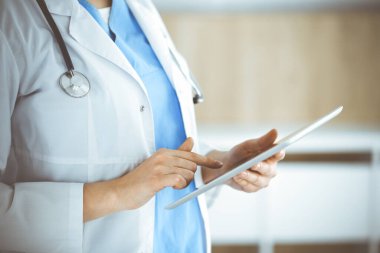 Bilinmeyen kadın doktor klinikte duruyor ve tablet bilgisayar kullanıyor, yakın plan. Tıp ve sağlık alanlarındaki veriler