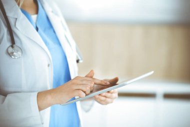 Bilinmeyen kadın doktor klinikte duruyor ve tablet bilgisayar kullanıyor, yakın plan. Tıp ve sağlık alanlarındaki veriler