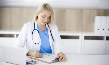 Hastanedeki ya da klinikteki masa başında oturan kadın doktor. Sarışın, neşeli doktor ilaç geçmişi formunu dolduruyor.