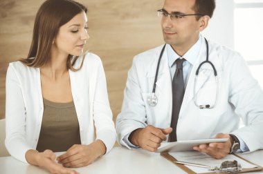 Doktor ve hasta klinikteki masada otururken tıbbi muayene sonuçlarını tartışıyorlar. Genç bir kadının ilaç geçmişini doldurmak için tablet bilgisayar kullanan bir erkek doktor. Tıptaki veriler