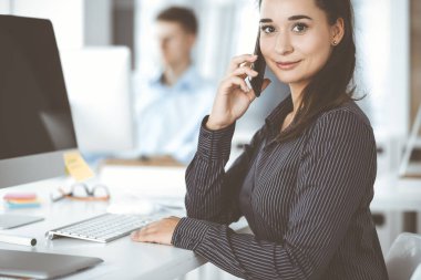 Modern ofisteki işyerinde bilgisayar kullanan bir iş kadını. Esmer sekreter ya da kadın avukat gülümsüyor ve mutlu görünüyor. Zevk ve başarı için çalışmak